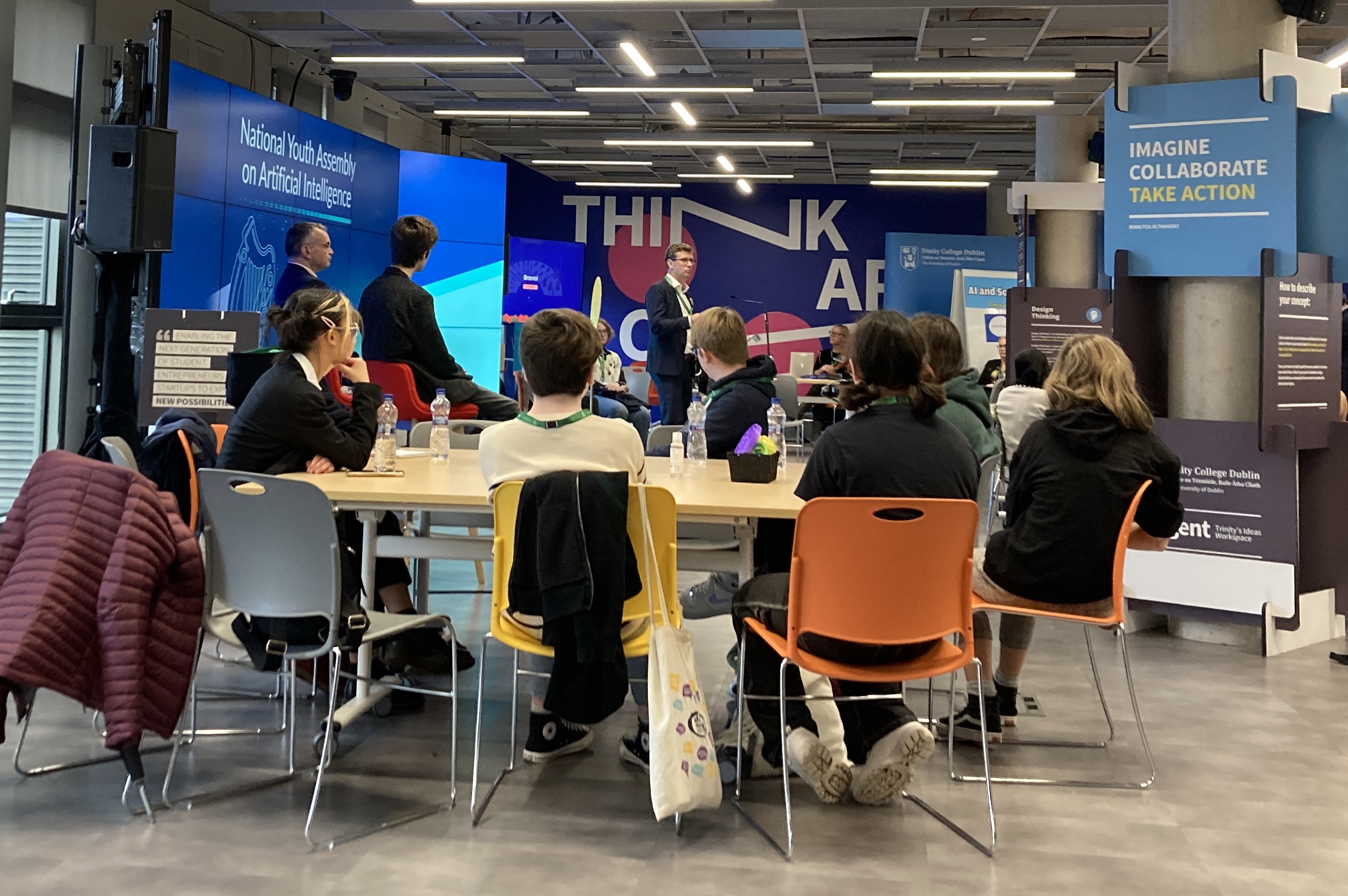 A group of young students sitting around a table listening to people talk about AI